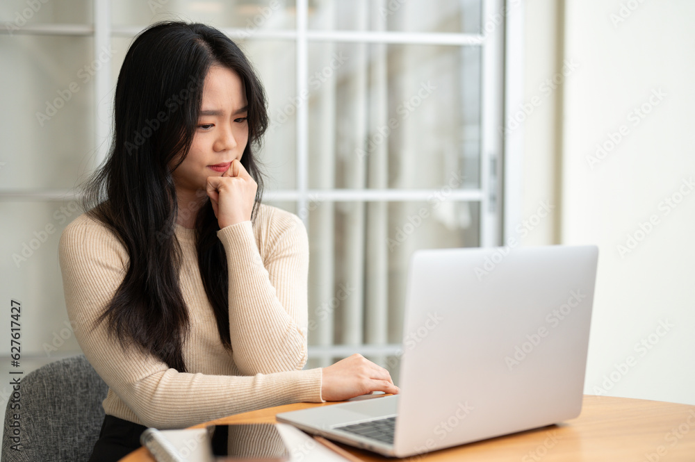 A thoughtful and doubtful Asian female college student reading an online research paper A thoughtful and doubtful Asian female college student reading an online research paper