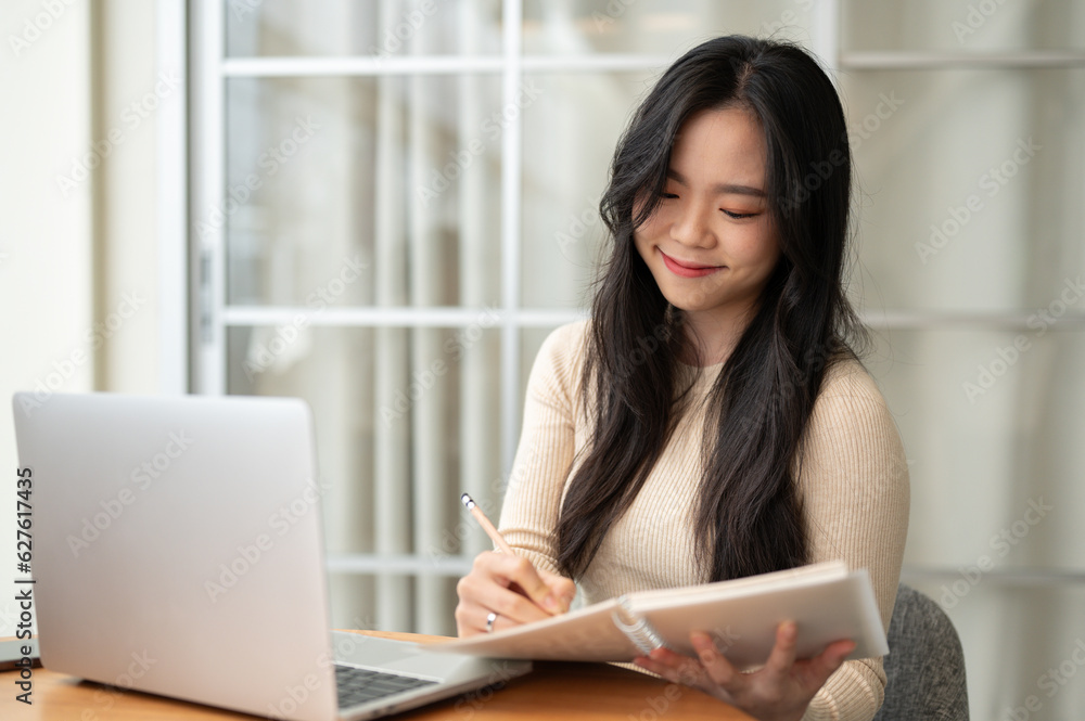 A happy young Asian female college student focuses on studying online at home. A happy young Asian female college student focuses on studying online at home.