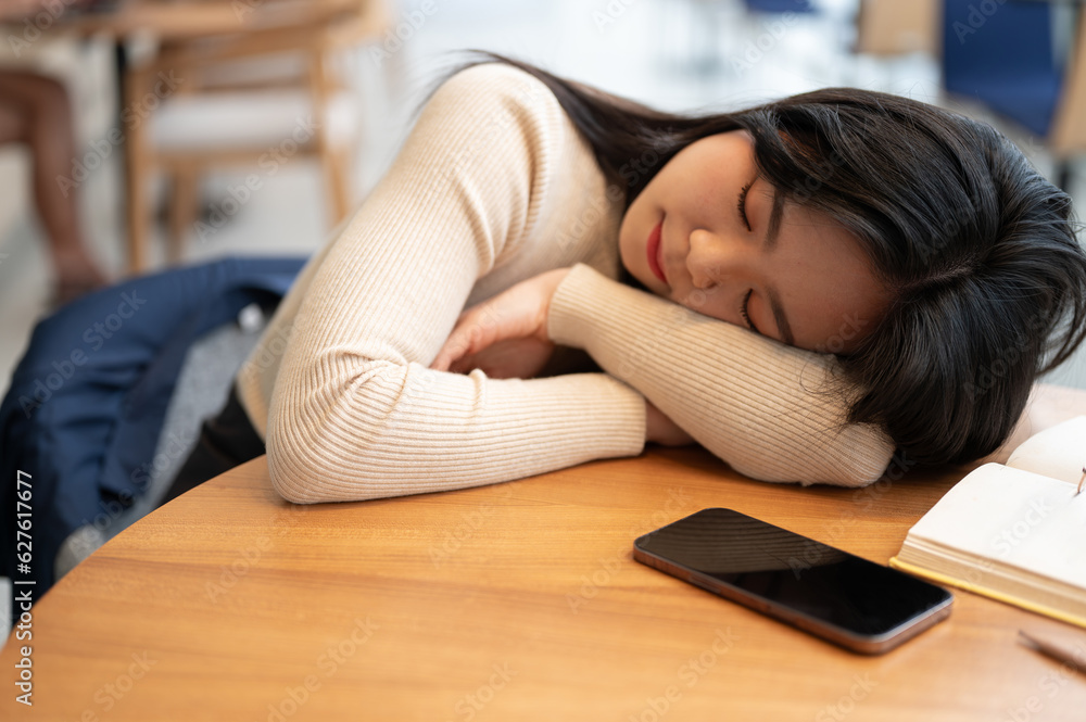 A beautiful young Asian woman is falling asleep on a table in a library or coffee shop. A beautiful young Asian woman is falling asleep on a table in a library or coffee shop.