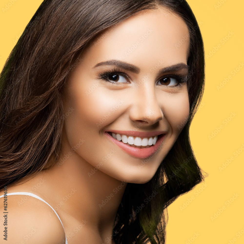 Obraz premium Portrait of smiling beautiful woman in white casual tank top looking at camera, over yellow color background. Brunette girl at studio concept. Square composition.
