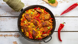 Homemade prepared paella with meat, pepper, vegetables and spices in iron pan on white peeling paint wooden planks, chili pepper on background, view from above