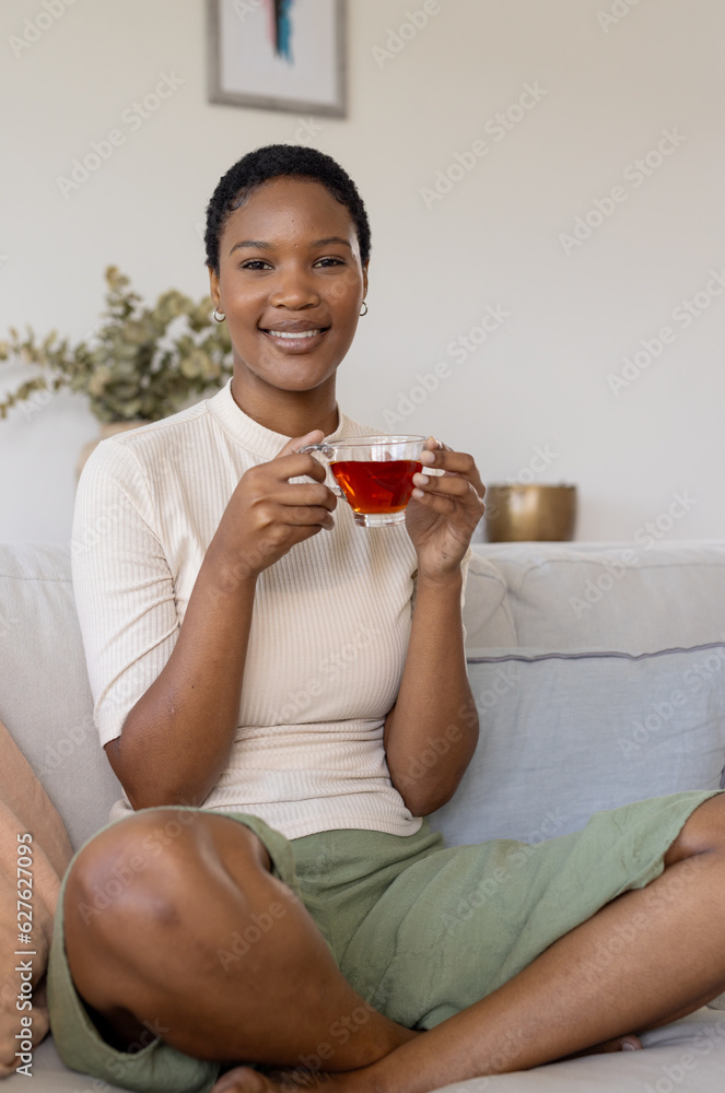 Portrait of happy african american woman sitting on sofa, holding cup of tea Portrait of happy african american woman sitting on sofa, holding cup of tea