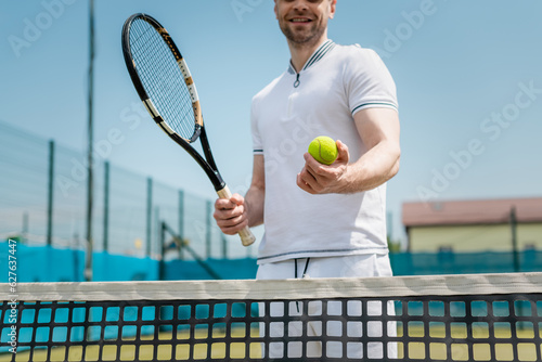cropped view of man in sportswear holding tennis racquet and ball near net, player, hobby and sport © LIGHTFIELD STUDIOS