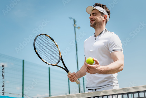 cheerful tennis player in visor cap holding racket and  ball on court, fitness and motivation, joy © LIGHTFIELD STUDIOS