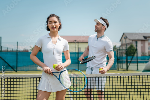 happy woman in active wear holding tennis racquet near man, tennis players on court © LIGHTFIELD STUDIOS