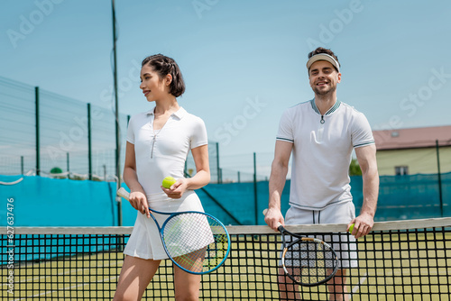 happy man and woman in sportswear standing with tennis rackets on court, fitness and health © LIGHTFIELD STUDIOS