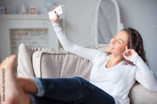 Relax in the rhythm of music. Attractive young woman lwith earphones and smartphone sitting on sofa at home. photo