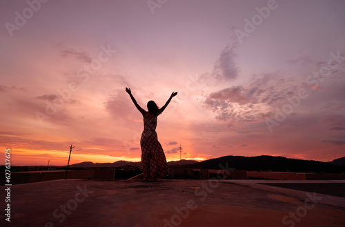 Young happy woman rising hands up enjoying beautiful sunset