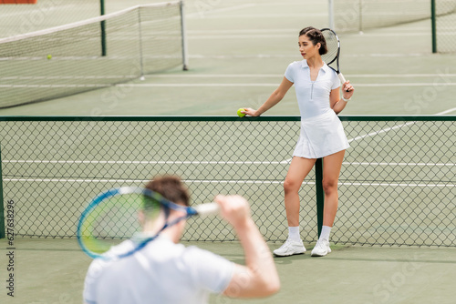 female tennis player standing near net and holding racket, man in active wear on blurred foreground © LIGHTFIELD STUDIOS