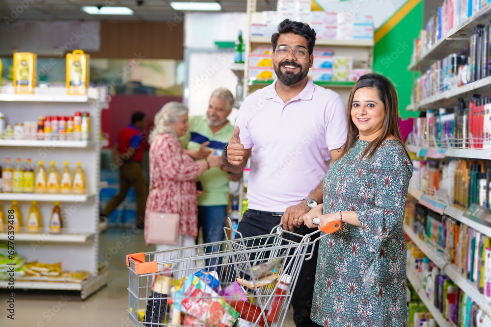 Happy indian couple doing shopping together and showing thumps up at grocery shop.
