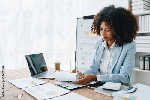 Beautiful young African american businesswoman using laptop computer and paperworks with planning working on financial document, tax, exchange, accounting and Financial advisor