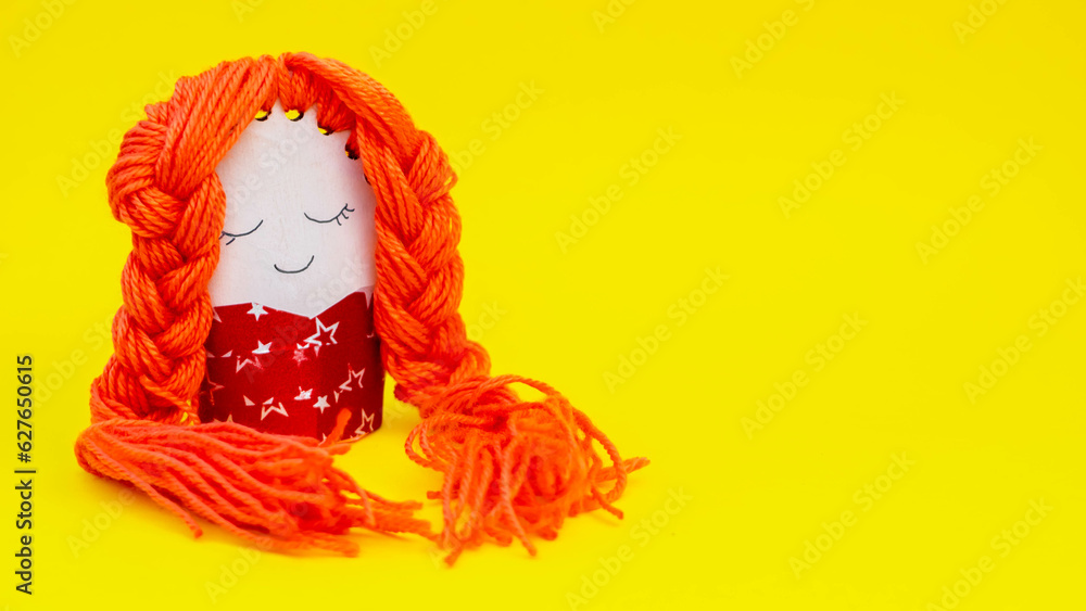 handmade doll with long orange hair on yellow background. children's crafts