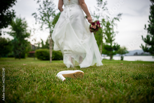 A bride leaving her shoe like Cinderella on a green nature field. Runaway bride concept. Names on the sole of the shoe tradition.. High quality photo