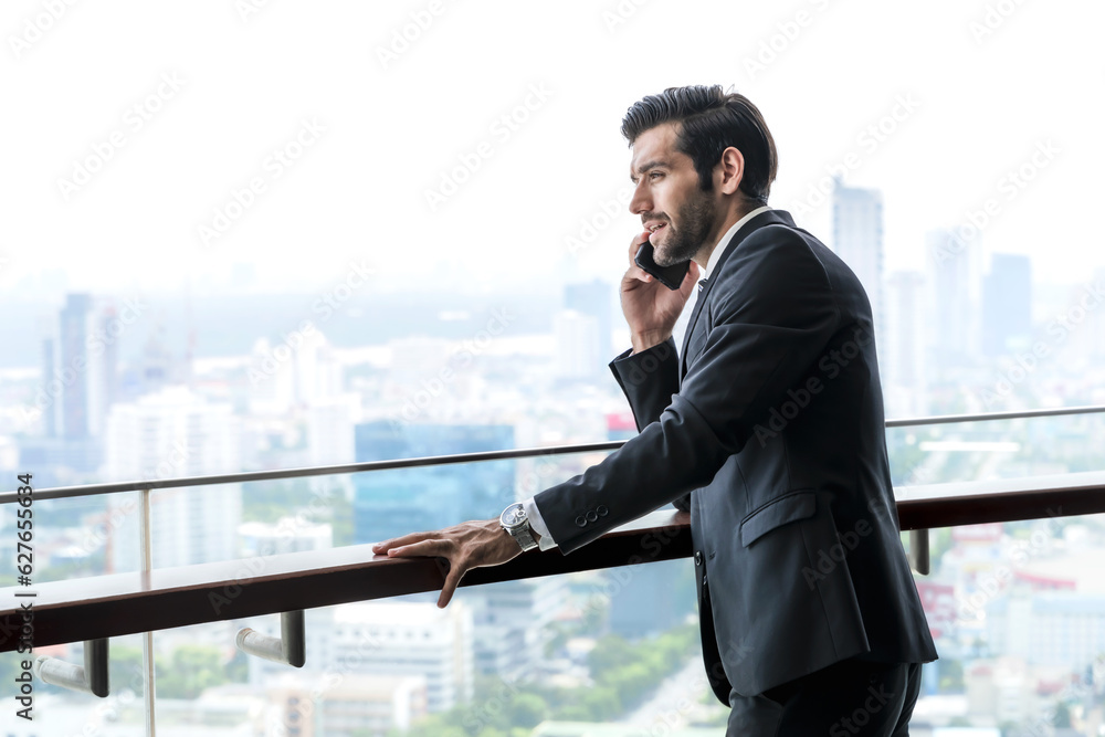 Caucasian businessman talking on cellphone at office balcony with cityscape background Caucasian businessman talking on cellphone at office balcony with cityscape background
