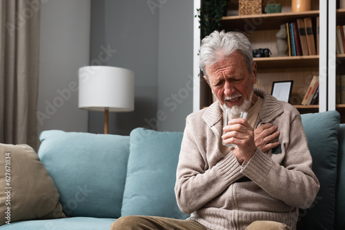 Tableau sur toile Senior older man getting chest pain in living room, heart attack holding his hand on the chest sitting on sofa at home