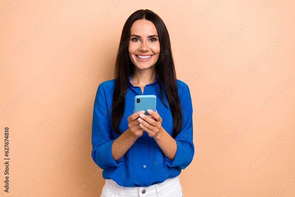 Photo of pretty lovely person beaming smile hold use smart phone chatting isolated on beige color background Photo of pretty lovely person beaming smile hold use smart phone chatting isolated on beige color background