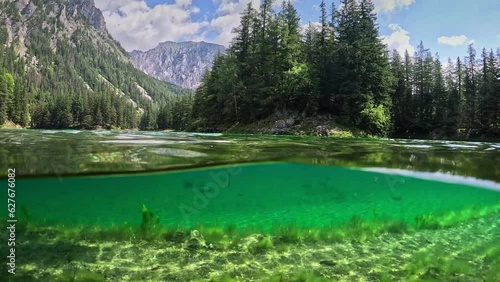 Half underwater shot of mountain lake with clear water in the Alps of Austria. Camera dive into the lake, rocky mountains and forest in the background. Alpine nature, Gruener See