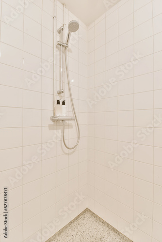 a white tiled bathroom with shower head and hand held in the shower arm, which is connected to the wall