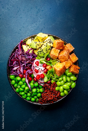 Vegan buddha bowl with red quinoa, fried tofu, avocado, edamame beans, green peas, radish, cabbage, pomegranate  and sesame seeds with soy sauce. Healthy diet food. Blue table background, top view photo
