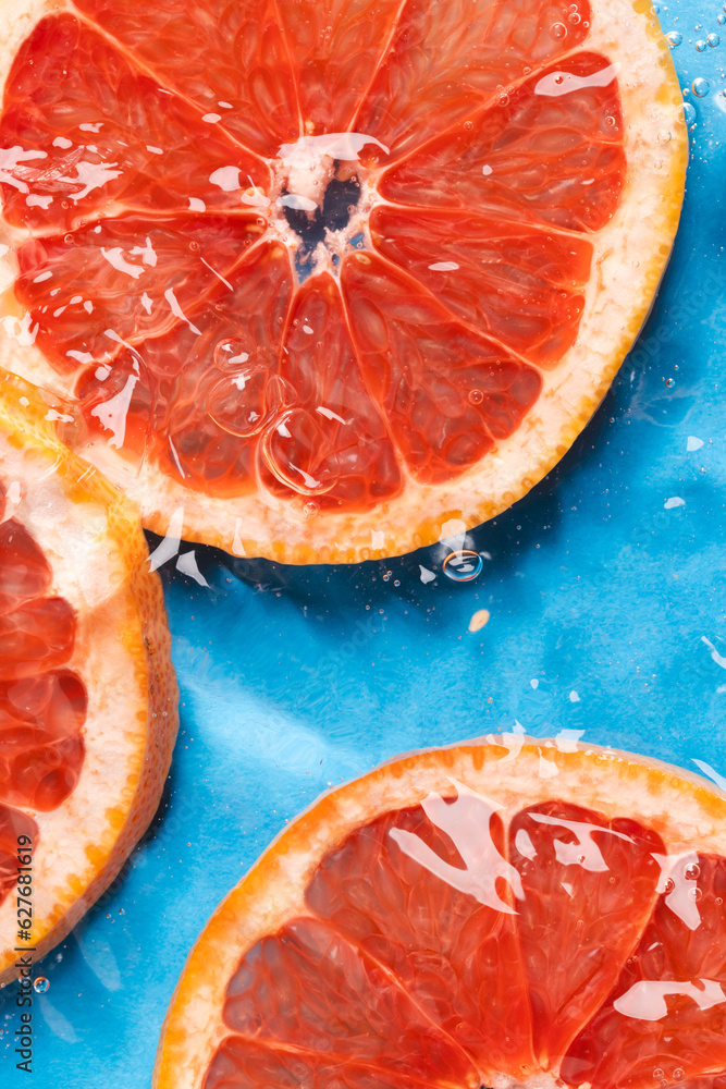 Close up of red grapefruit slices in water with copy space on blue background Close up of red grapefruit slices in water with copy space on blue background