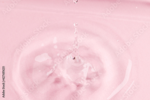 Close up of water drop falling into water with ripples and copy space on pink background