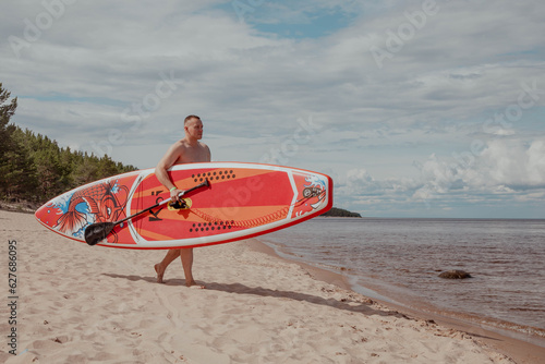 Man walks along the beach with sup board