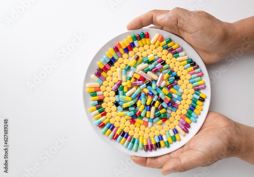 Multi-colored pills on a white plate and two hands