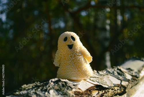 A smiling ghost toy close-up stands on a birch bark in the forest and sunlit
