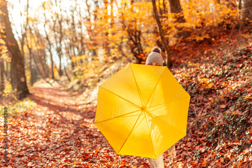 Woman hiding behind umbrella while taking a walk through forest