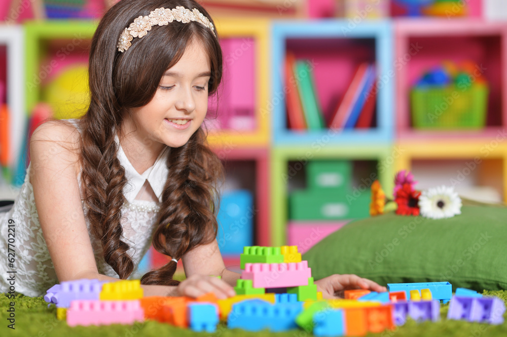 Fototapeta premium Portrait of cute girl playing with colorful plastic blocks in room