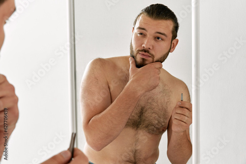 One man with tweezer toching his beard and looking at mirror. Male facial care. Bearded man. photo