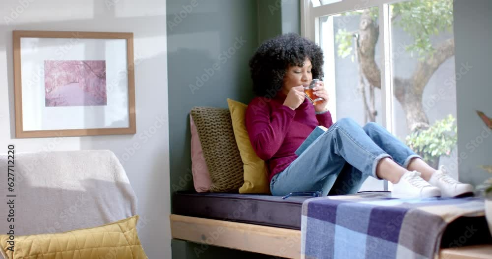 Biracial woman drinking tea and reading book at home, slow motion Biracial woman drinking tea and reading book at home, slow motion