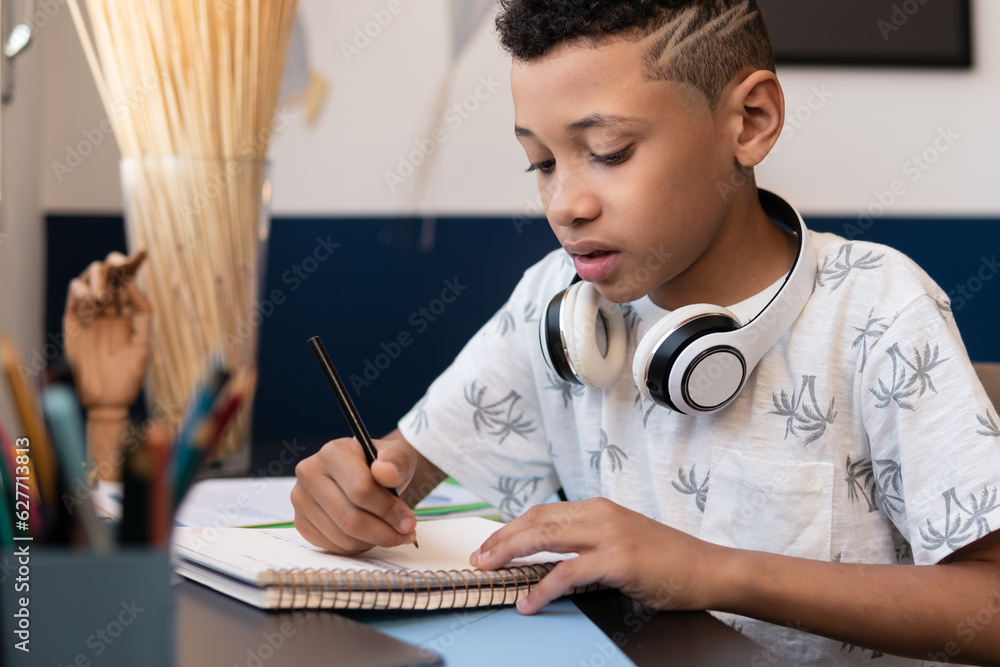 Studious boy writes in school notebook at desk in room Studious boy writes in school notebook at desk in room