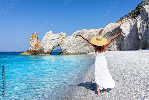 A elegant tourist woman in a white summer dress enjoys the beautiful beach of Lalaria, Skiathos island, Greece, during sunset time photo