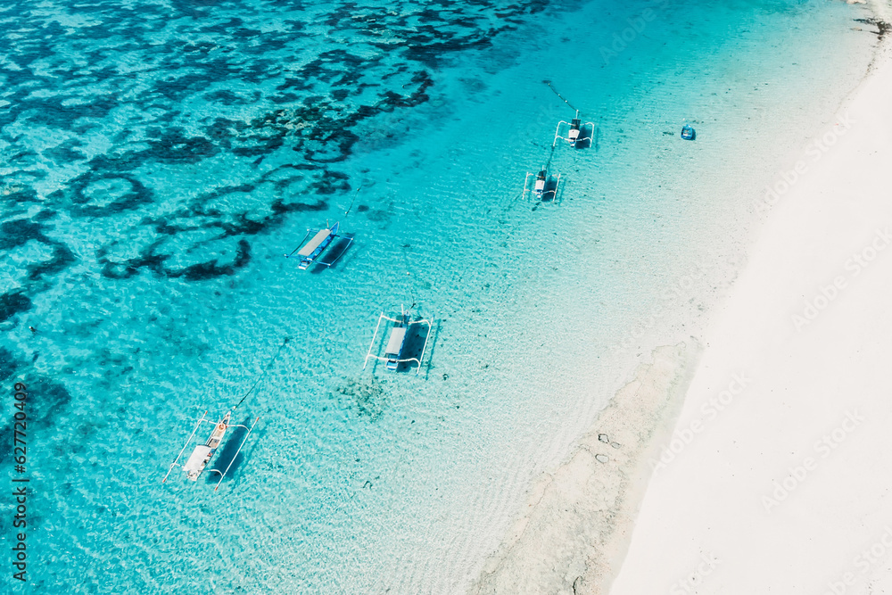 Transparent ocean and beach with fishing boats in tropical island. Aerial view.