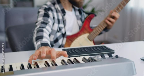 Close up of male hands playing on syntezator playing and guitar. Bearded musician man in headphone recording a song while using synthesizer and guitar at home studio photo