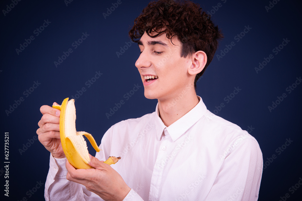 Funny emotional guy eats a banana. Student posing on a blue background. Funny emotional guy eats a banana. Student posing on a blue background.