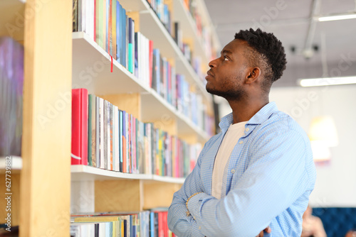 Black man standing in front of a bookshelf and looking at books