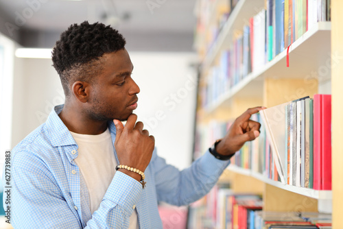African student standing in front of a bookshelf and pointing at a book