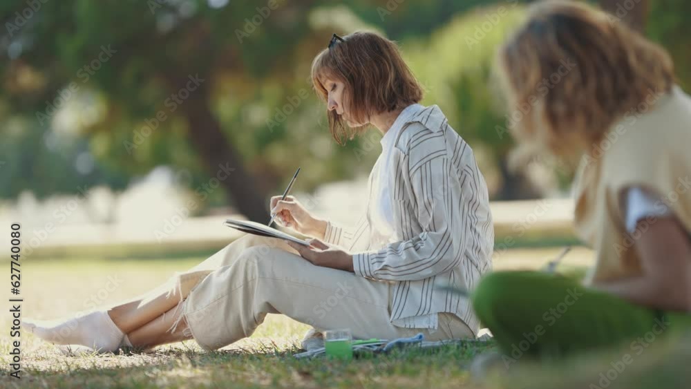 Two women friends painting with watercolors and talking in the park Two women friends painting with watercolors and talking in the park