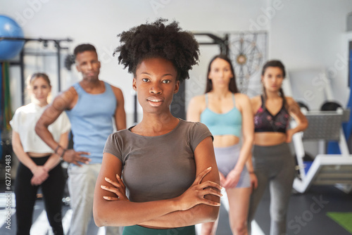 Confident woman while posing in front of a group of sporty people in the gym. Sports concept.