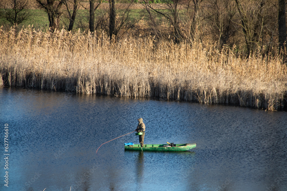 Lonely fisherman on the green wooden boat fishing with fisherman's stick, enjoying the nature and calm waters of small river Lonely fisherman on the green wooden boat fishing with fisherman's stick, enjoying the nature and calm waters of small river