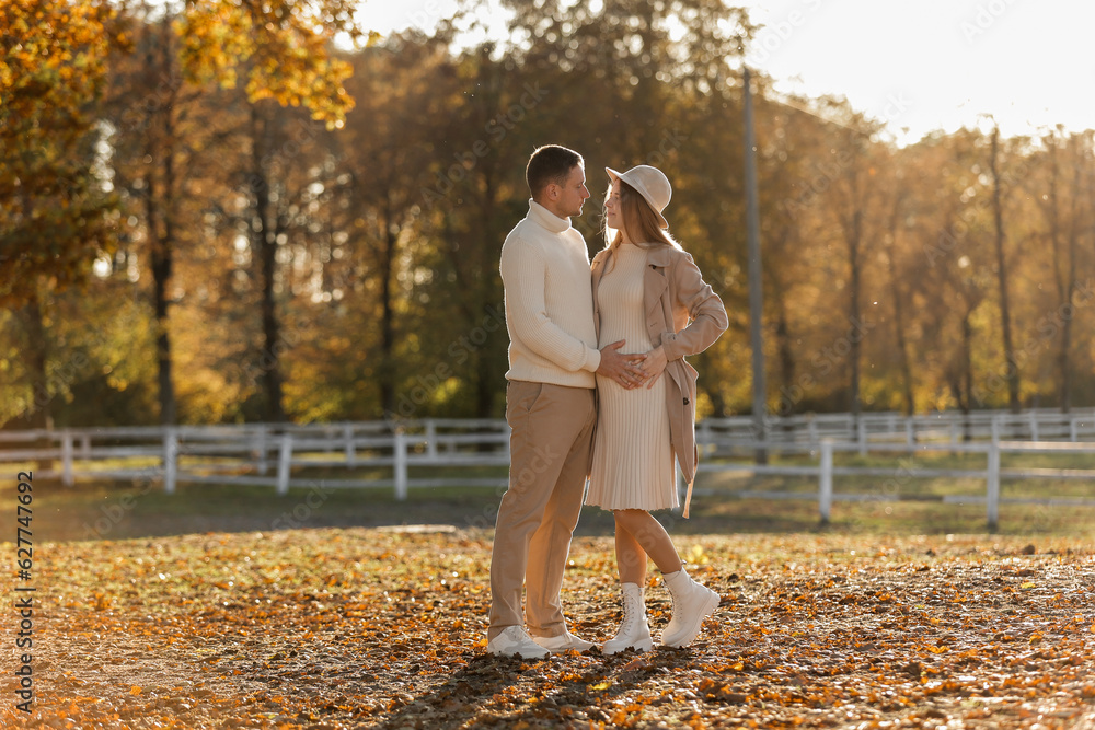 Fototapeta premium Young stylish couple lovers are hugging and kissing in the autumn park. Lovely romantic moment between man and woman in love, looking to each others. Happy family. Love, youth, happiness concept.