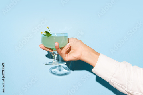 Women hand holding glass with margarita cocktail on light blue pop art background. Copy space for ad.
