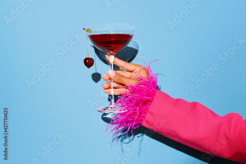 Women hand holding glass with drunk cherry cocktail over blue pop art background. Copy space for ad.