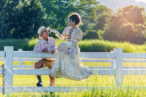 Schilderij op canvas Teenage girl and boy in ancient-style costumes relaxing happy together at White fence in sheep pasture