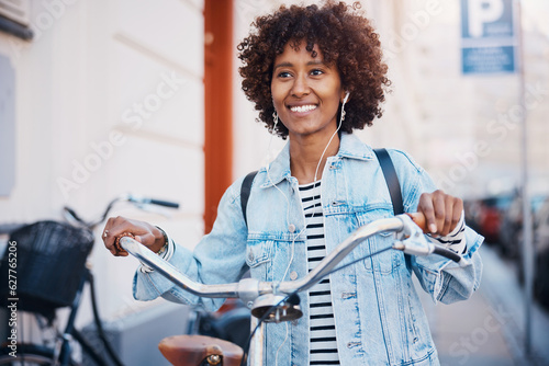 Smiling woman wearing headphones pushing a bike along a sidewalk in the city