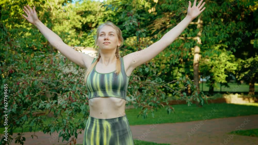 Sporty woman raising arms up and stretching in park. Flexible female practicing yoga. Girl in sportswear exercises outdoors for health and wellbeing
