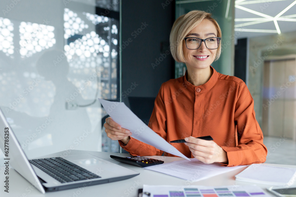 Young successful business woman working inside office with documents, woman satisfied with achievement results reviewing contract, bills and documents, financier in glasses smiling. - obrazy, fototapety, plakaty 