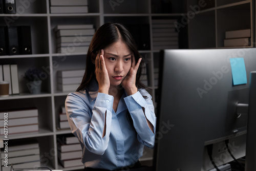 Stressful Asian businesswoman having a headache while working overtime at night, feeling tired after a long day at work.